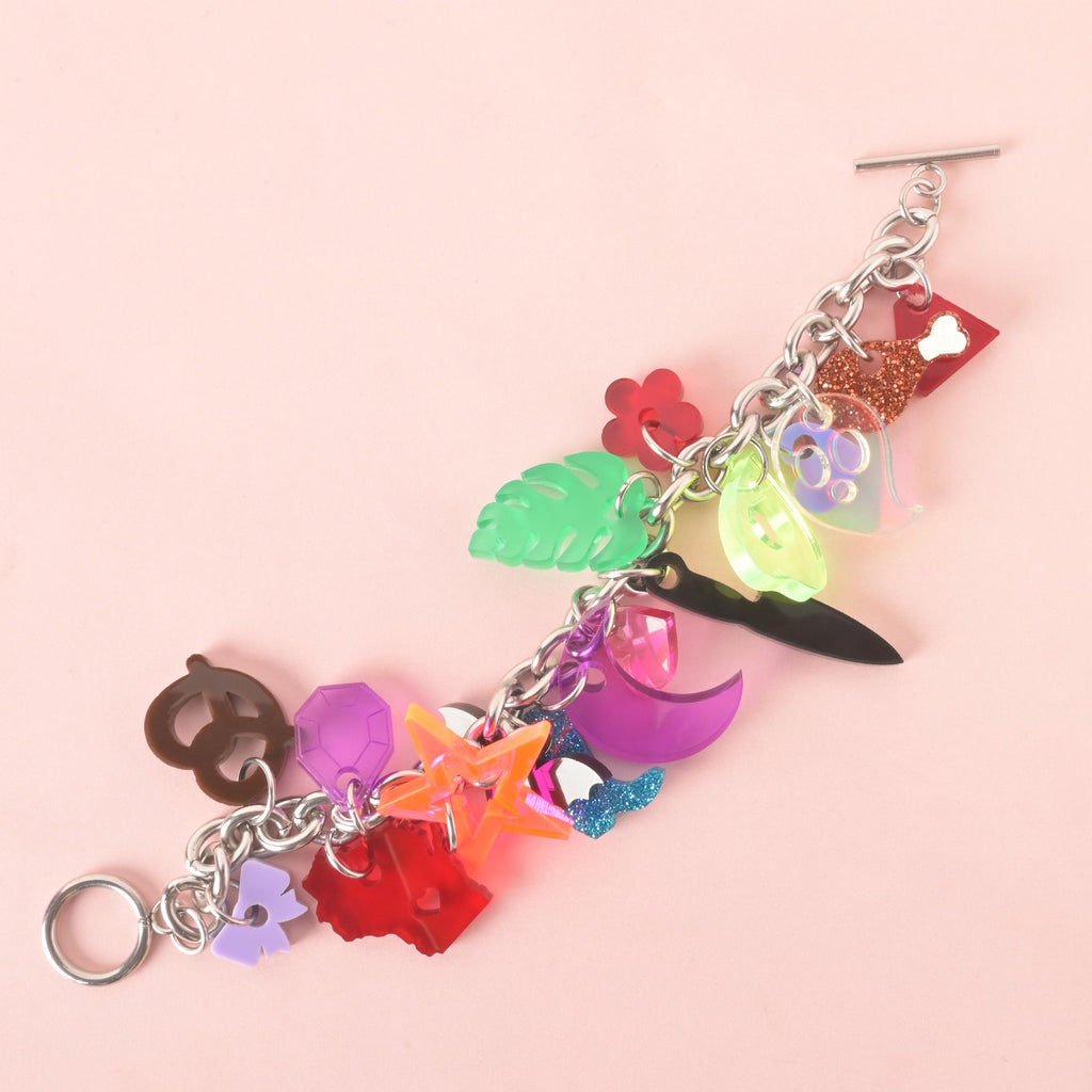 Colorful acrylic charm bracelet with bold charms including a red Wisconsin state with heart cutout, pizza slice, ghost, avocado, tropical leaf, pretzel, moon, star, and bow, all on a silver chain.