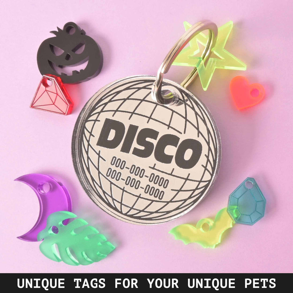A silver circular pet ID tag featuring a 'DISCO' globe design and phone numbers. It is surrounded by various small, colorful acrylic charms/mini-tags, including a jack-o'-lantern, gem, neon star, heart, crescent moon, monstera leaf, and bat shapes. Large Disco Pet tag, Mirror Disco Personalized Pet Tag the Clifford Series, for big dog, extra strong ID Tag