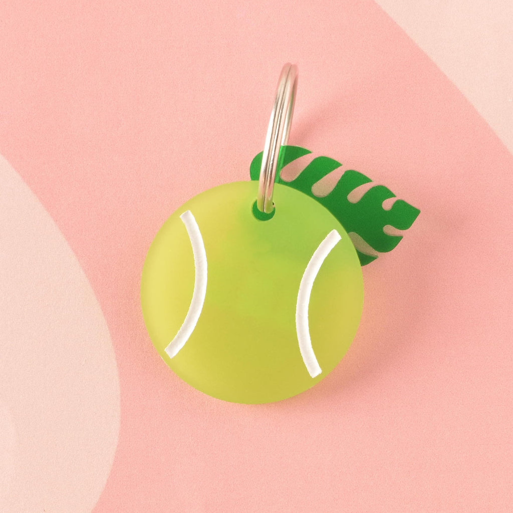 A circular acrylic charm shaped like a tennis ball in frosted lime green with white markings, accented with a dark green tropical leaf charm. Ideal as a colorful pet collar accessory.Tennis Ball Pet Tag, Personalized Pet tag, Cat or Dog ID Tag, summer ball tag