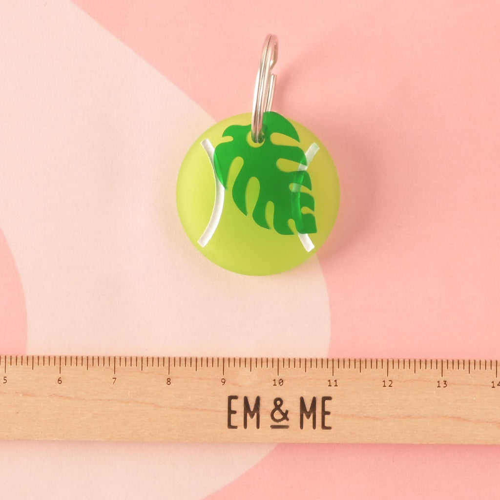 A circular acrylic charm shaped like a tennis ball in fluorescent neon green with white markings, accented with a dark green tropical leaf charm. Ideal as a colorful pet collar accessory. Tennis Ball Pet Tag, Personalized Pet tag, Cat or Dog ID Tag, summer ball tag