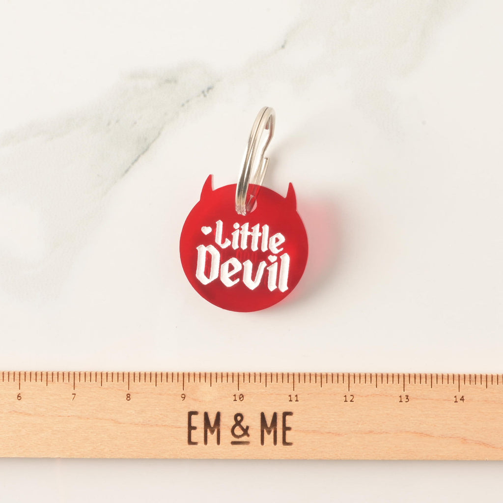 Little Devil Red Pet Tag for Dogs and Cats, Close up with wooden ruler that reads "EM & ME" on marble background.