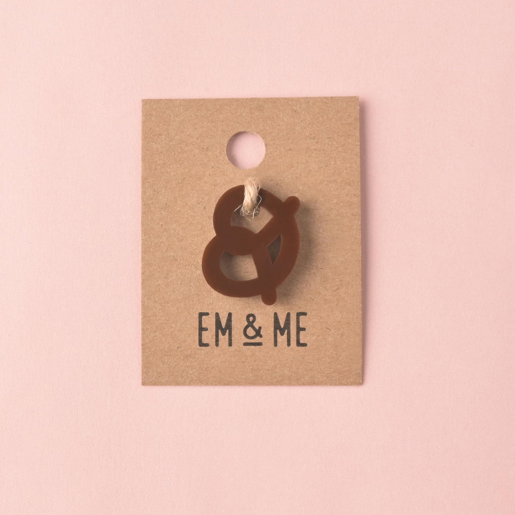 Brown pretzel mini pet charm packaged on kraft paper card on solid pink background