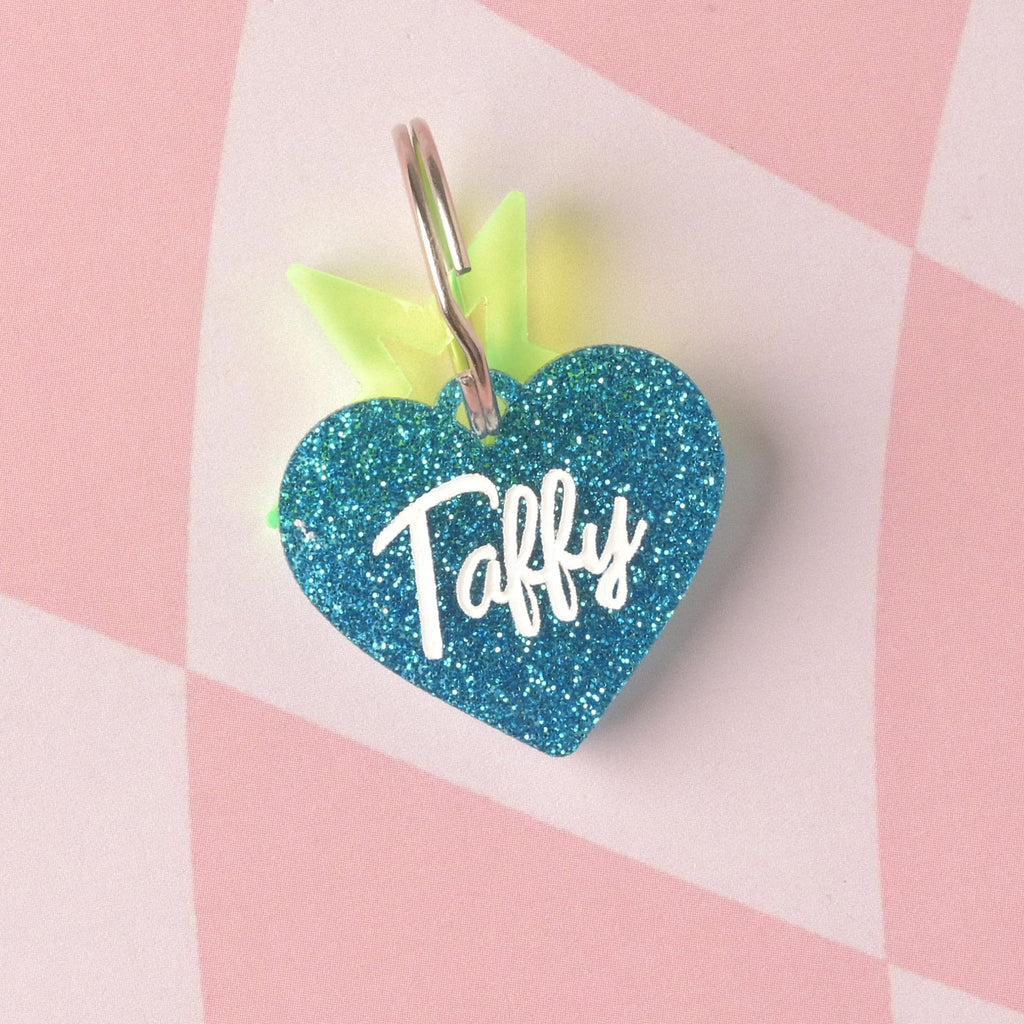 A custom heart-shaped pet ID tag made from vibrant blue glitter acrylic. The tag is engraved with the name 'Taffy' in white script and is accented with a fluorescent neon yellow-green charm partially visible behind the heart. Barbie Inspired Personalized Pet Tag, Taffy Heart Shaped Tag for Cats and Dogs, Limited Edition, Custom Name and Contact Info Engraved
