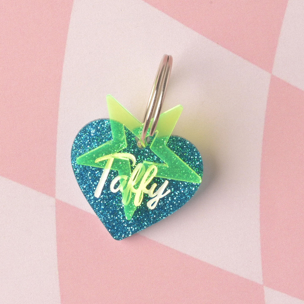 custom heart-shaped pet ID tag made from vibrant blue glitter acrylic. The tag is engraved with the name 'Taffy' in white script and accented with a fluorescent neon yellow-green star charm on a split ring. Barbie Inspired Personalized Pet Tag, Taffy Heart Shaped Tag for Cats and Dogs, Limited Edition, Custom Name and Contact Info Engraved