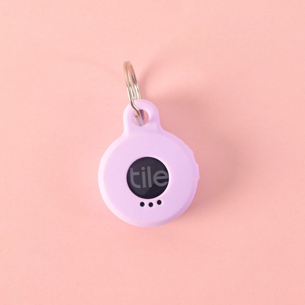 A personalized purple round silicone tag designed to hold a Tile tracker. The tag says "CHEESE" and has a placeholder phone number on it.  Back of Tag The tag is attached to a silver ring and is displayed on a solid pink background.