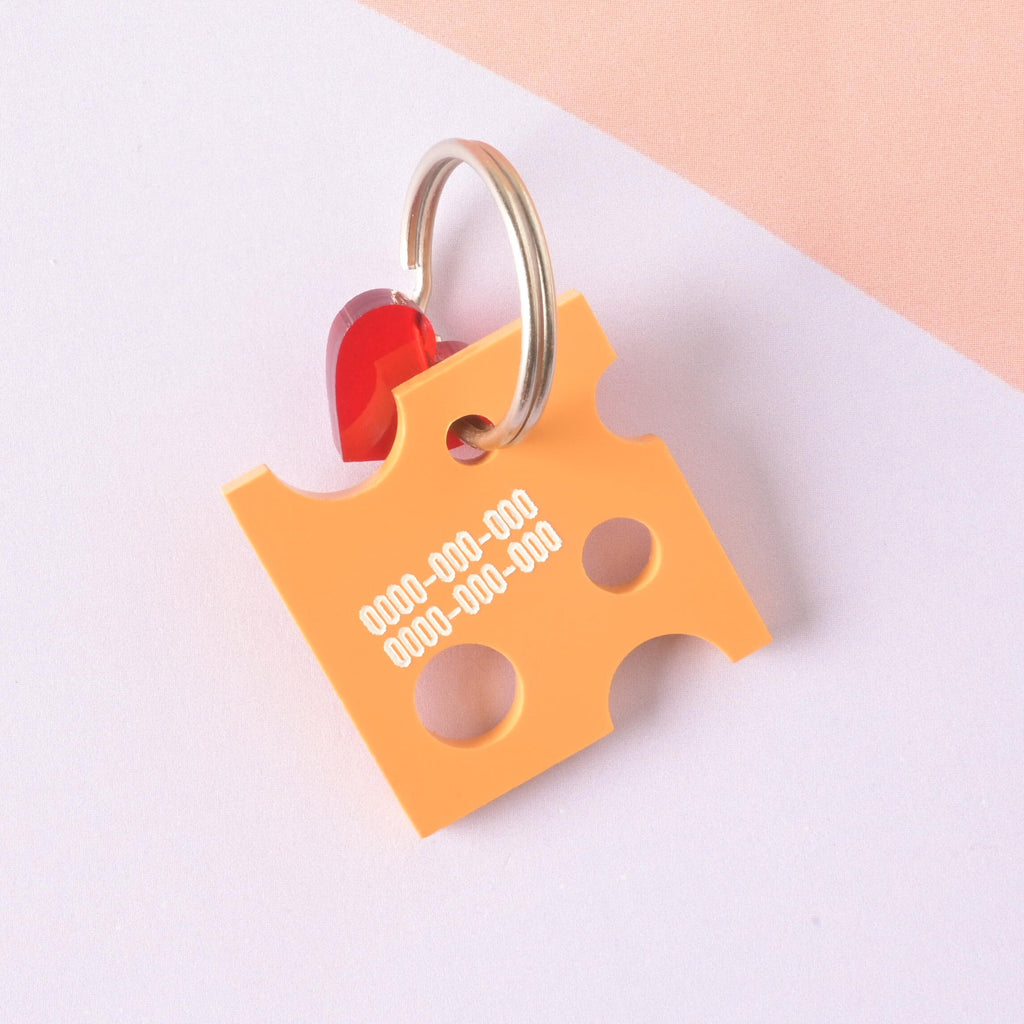 A custom pet ID tag shaped like a slice of Swiss cheese (orange acrylic) with "holes" cut out. The tag is engraved with phone numbers and accented with a small red heart charm, attached to a gold split ring. Personalized Cheese Pet Tag - Custom Tag for Cheese Lovers, dogs and cats - Engraved ID Name and Contact Info Included