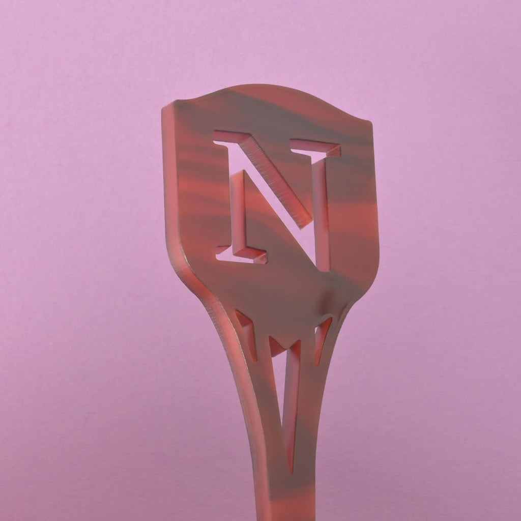 Personalized Family Shield Stir Sticks, Family Letter Initial Swizzle Sticks, Thanksgiving Bar cart, Stocking Stuffer A close-up of a dark red and black marbled cocktail stirrer featuring the cutout monogram letter 'N' at the top. The stirrer has a pointed shield shape and is viewed against a solid pink background.