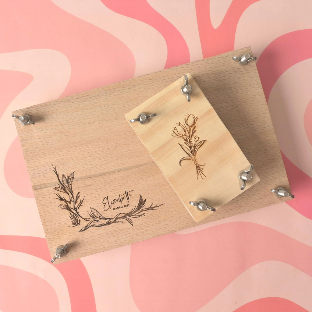 Large oak flower press kit and pocket press with personalized engraving of name and floral design, secured with screws and wing nuts on a pink background