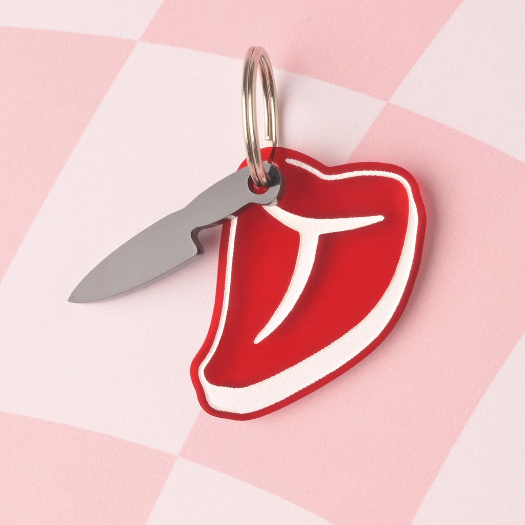 A personalized pet ID tag shaped like a red steak with white internal details, attached to a small, silver-colored metal knife charm. The tags are displayed on a pink and white checkered background. fake knife, Seasonal Mini,  Tiny Accessory for Pet ID Tag, Cats and Dogs Add-on Charm