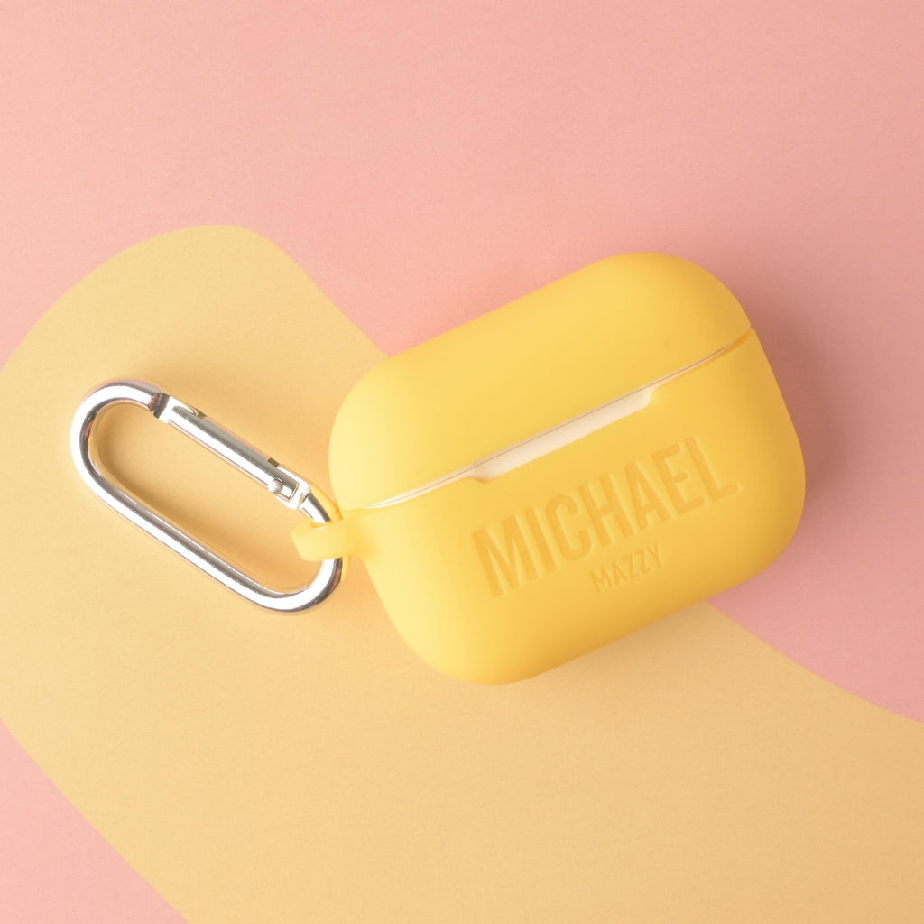 A personalized silicone AirPods Pro case in sunny yellow, custom engraved with the names 'MICHAEL' and 'MAZZY,' and featuring a silver metal carabiner clip.