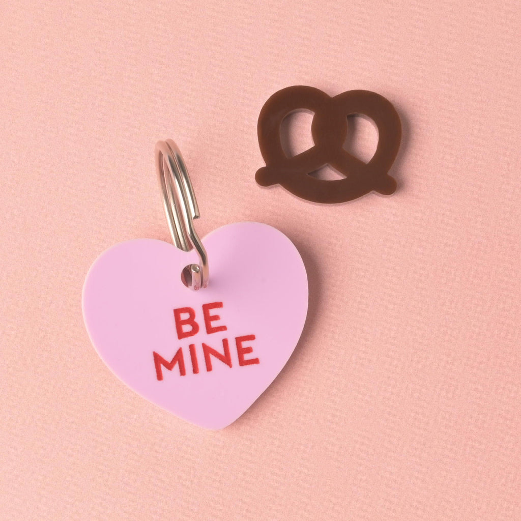 Pretzel, Seasonal Mini, Tiny Accessory for Pet ID Tag, next to lavender conversation heart pet tag on pink background