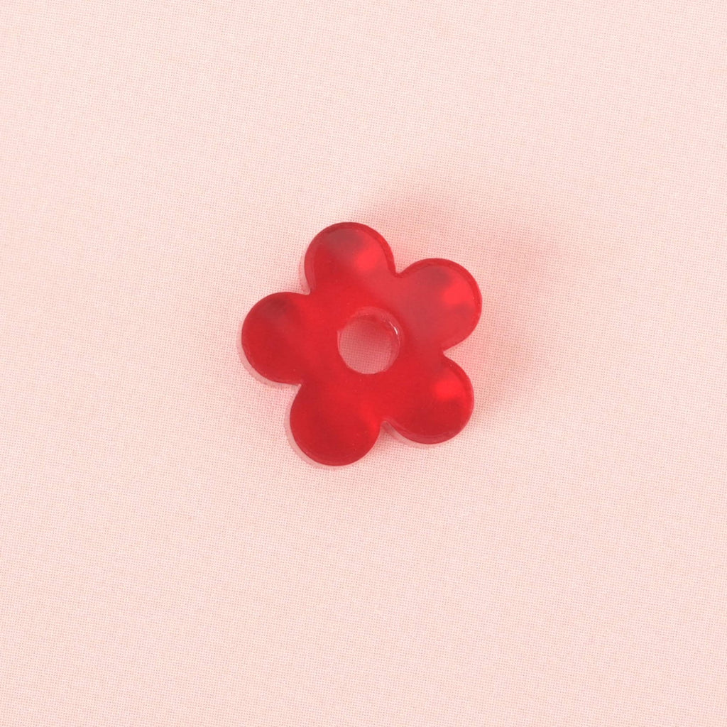 A single red, flower-shaped charm with a hole in the middle. The item is shown on a solid pink background.
