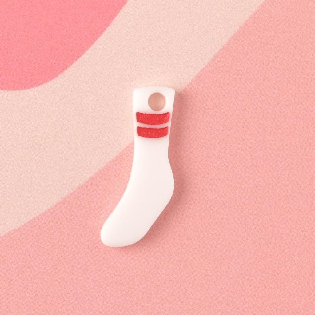 Tubesock, Missing Sock, Seasonal Mini, Tiny Accessory for Pet ID Tag, Cats and Dogs Add-on Charm A small, opaque white acrylic mini charm shaped like a tube sock, featuring two bold red glitter stripes near the top, displayed on a pink background.