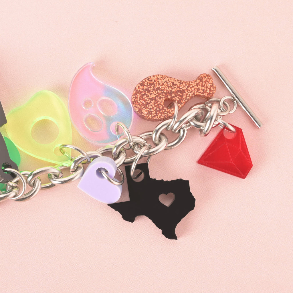 Acrylic charm bracelet with colorful shapes including a black Texas state charm with heart cutout, red gem, chicken leg, ghost, avocado, and pastel heart on a silver chain.