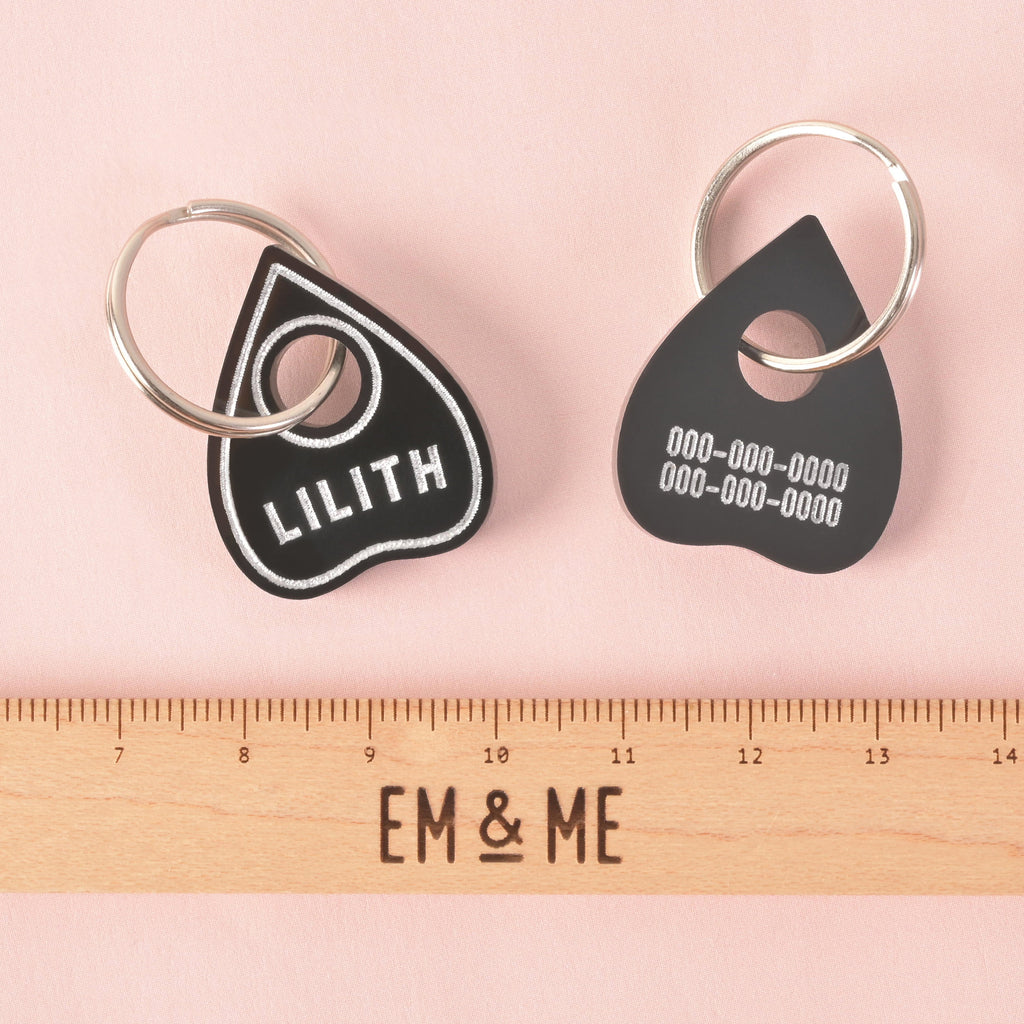 Black planchette pet ID tag showing the name LILITH on the front and phone numbers on the back, next to a ruler for scale. Gothic, spooky, and personalized dog tag. Small Ouijia Planchette Pet tag, Tiny Tag, Spooky Halloween Cat or small dog breeds, XS personalized pet name tag