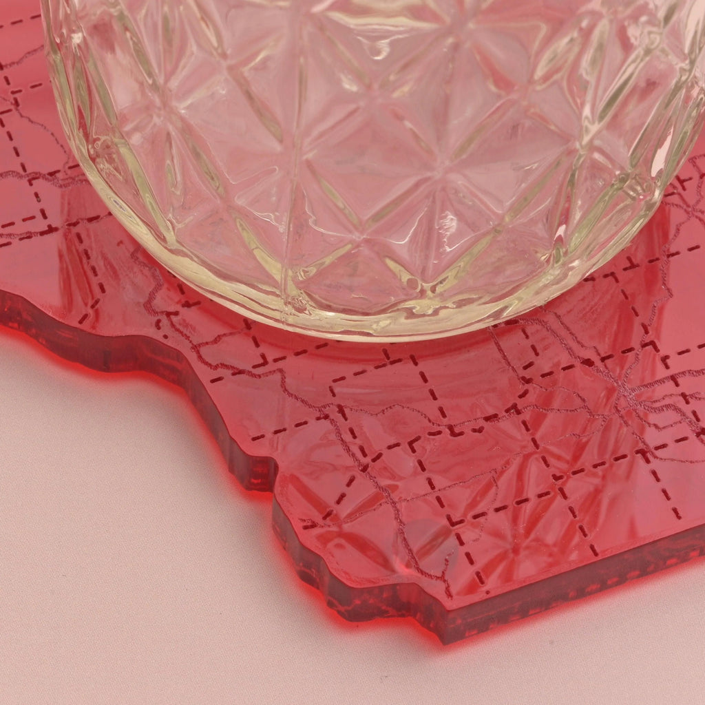 Close-up of a textured glass resting on a red acrylic Wisconsin-shaped coaster with detailed etched road map lines, highlighting the engraved surface and material quality.