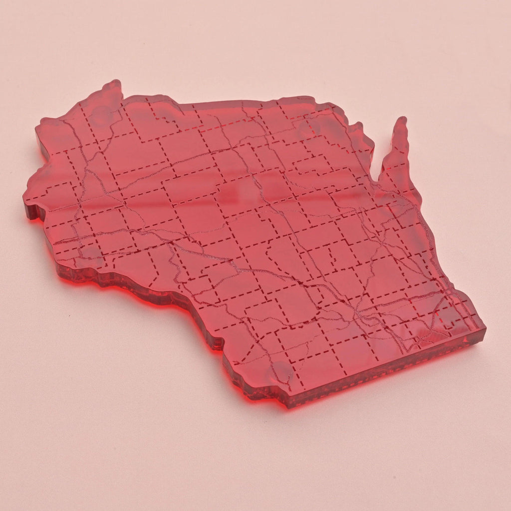 Red acrylic coaster in the shape of Wisconsin with etched road map design, shown flat against a blush pink background.