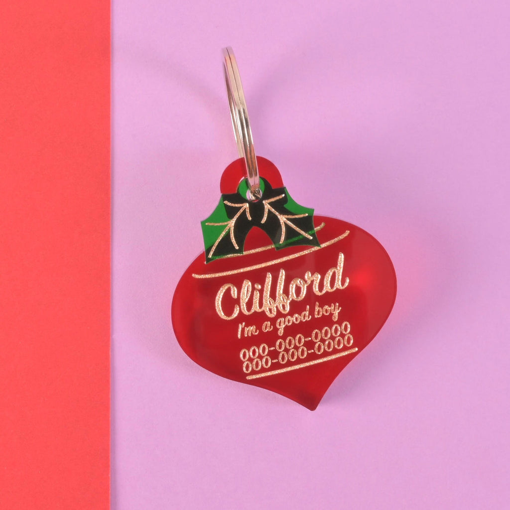 Red ornament-shaped acrylic dog tag with green holly detail and gold engraving for Clifford – personalized Christmas pet ID tag