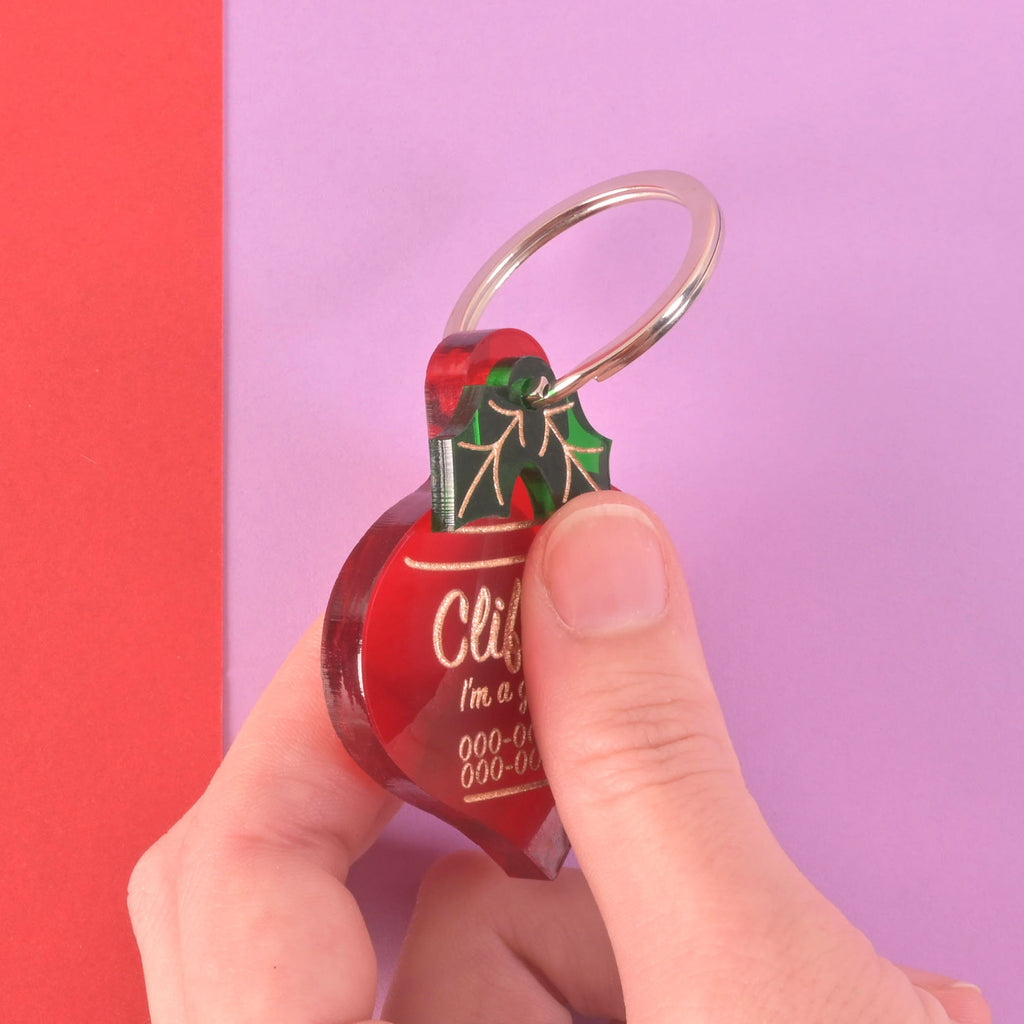 Close-up of hand holding Clifford red Christmas ornament dog tag showing its thick layered acrylic design and sturdy build quality