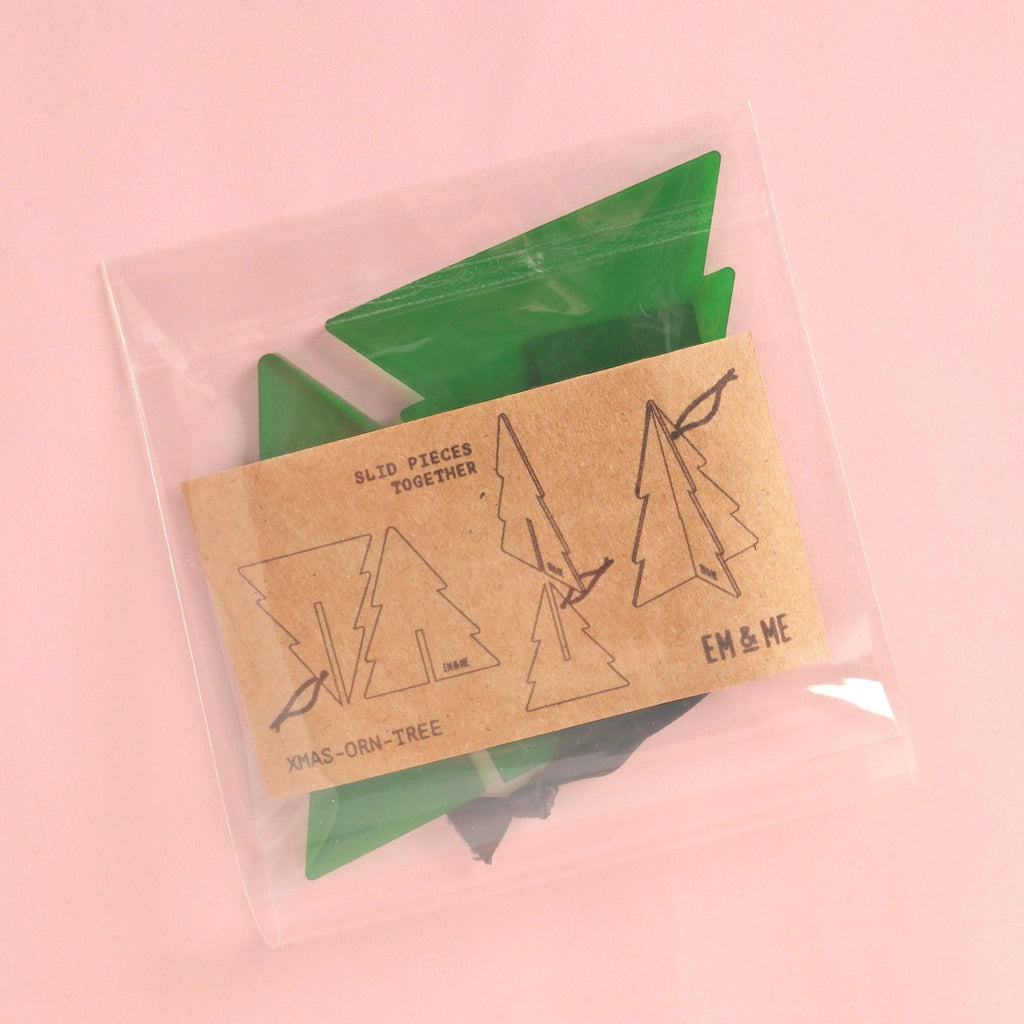 Clear bag with green acrylic tree pieces and kraft instruction card; DIY 3D Christmas tree ornament kit, flat-pack parts shown in packaging, ready to assemble.