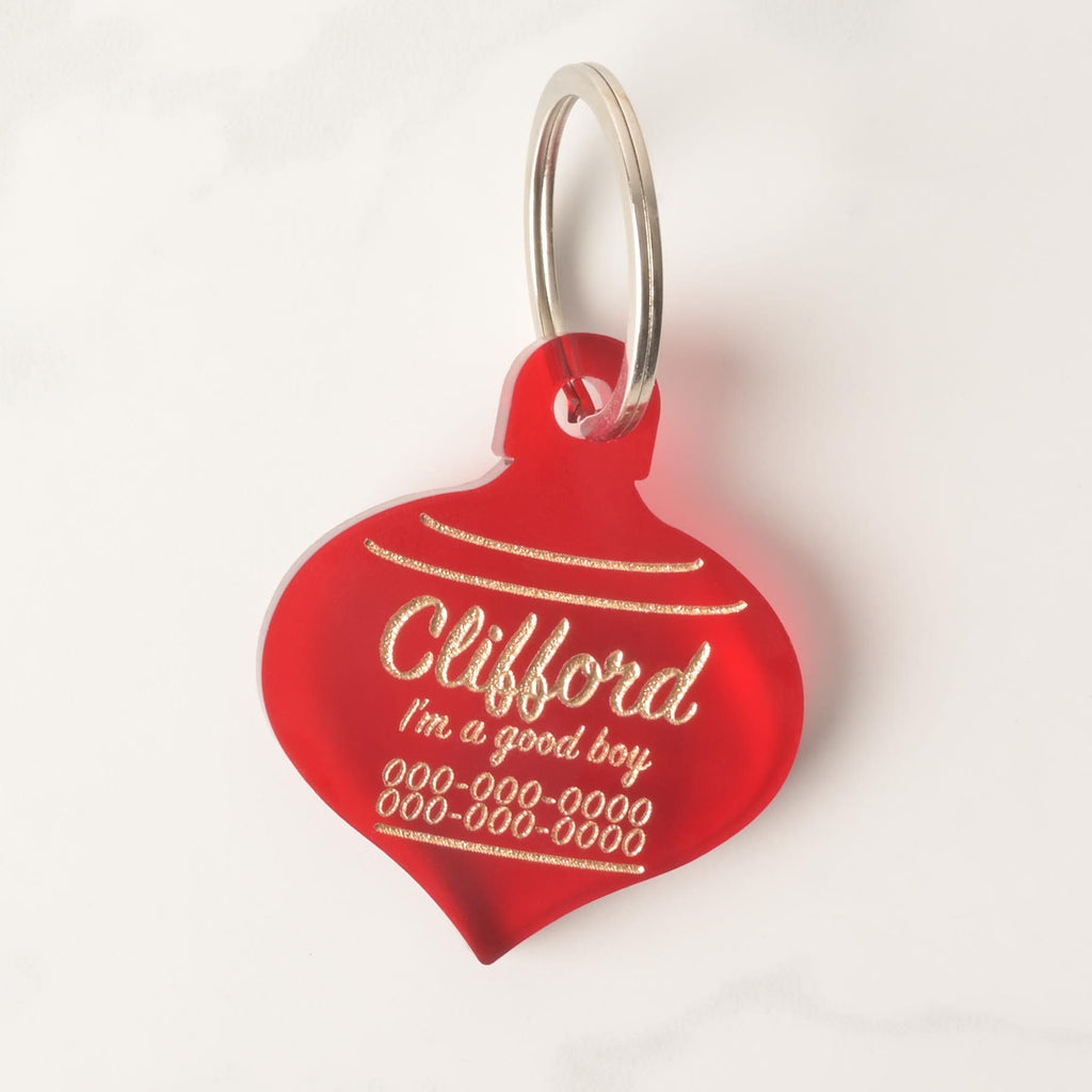 Close-up of red acrylic Christmas ornament-shaped dog tag with gold engraving and custom name Clifford – festive personalized pet ID tag
